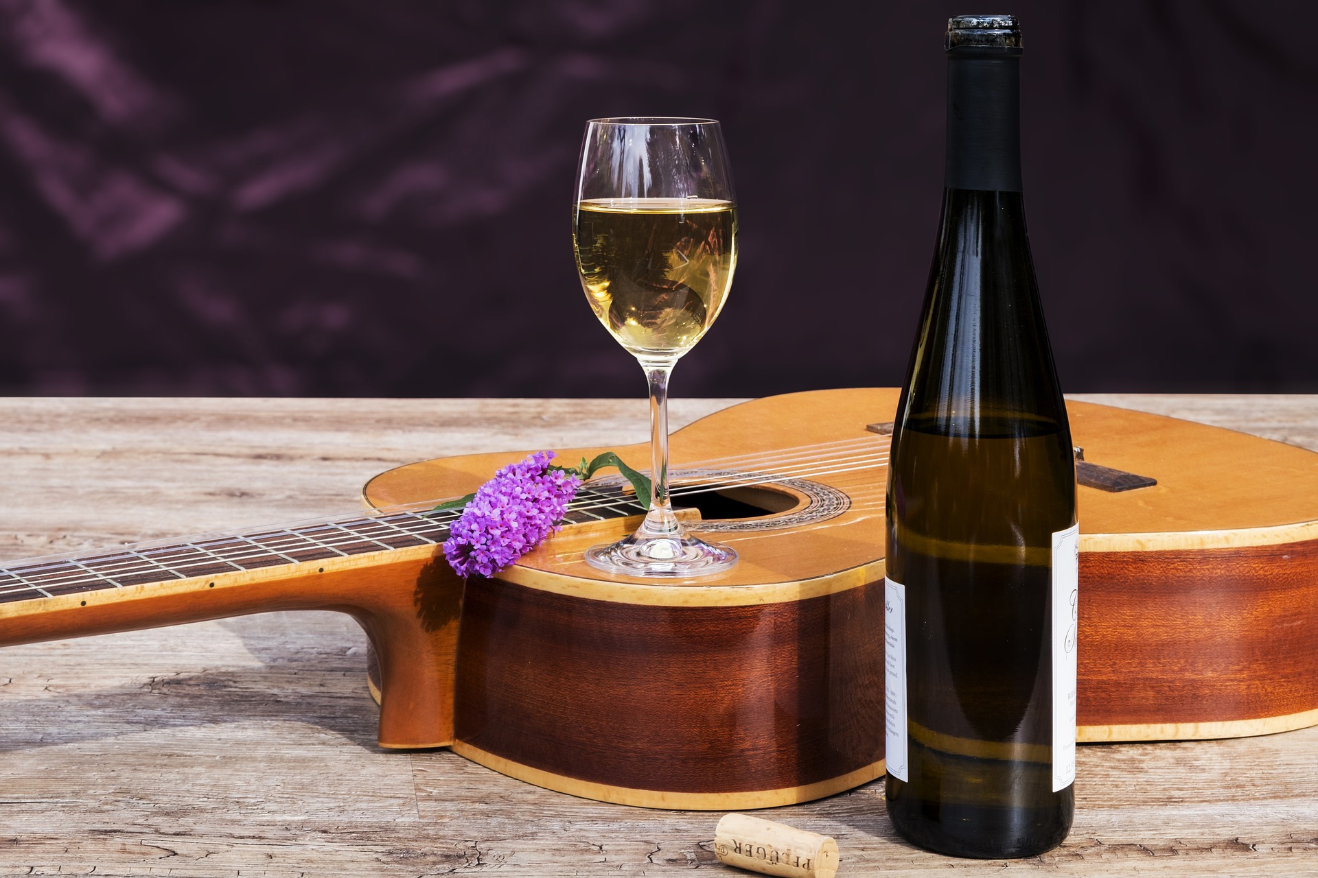 Glass of white wine sitting on a guitar with lilacs.